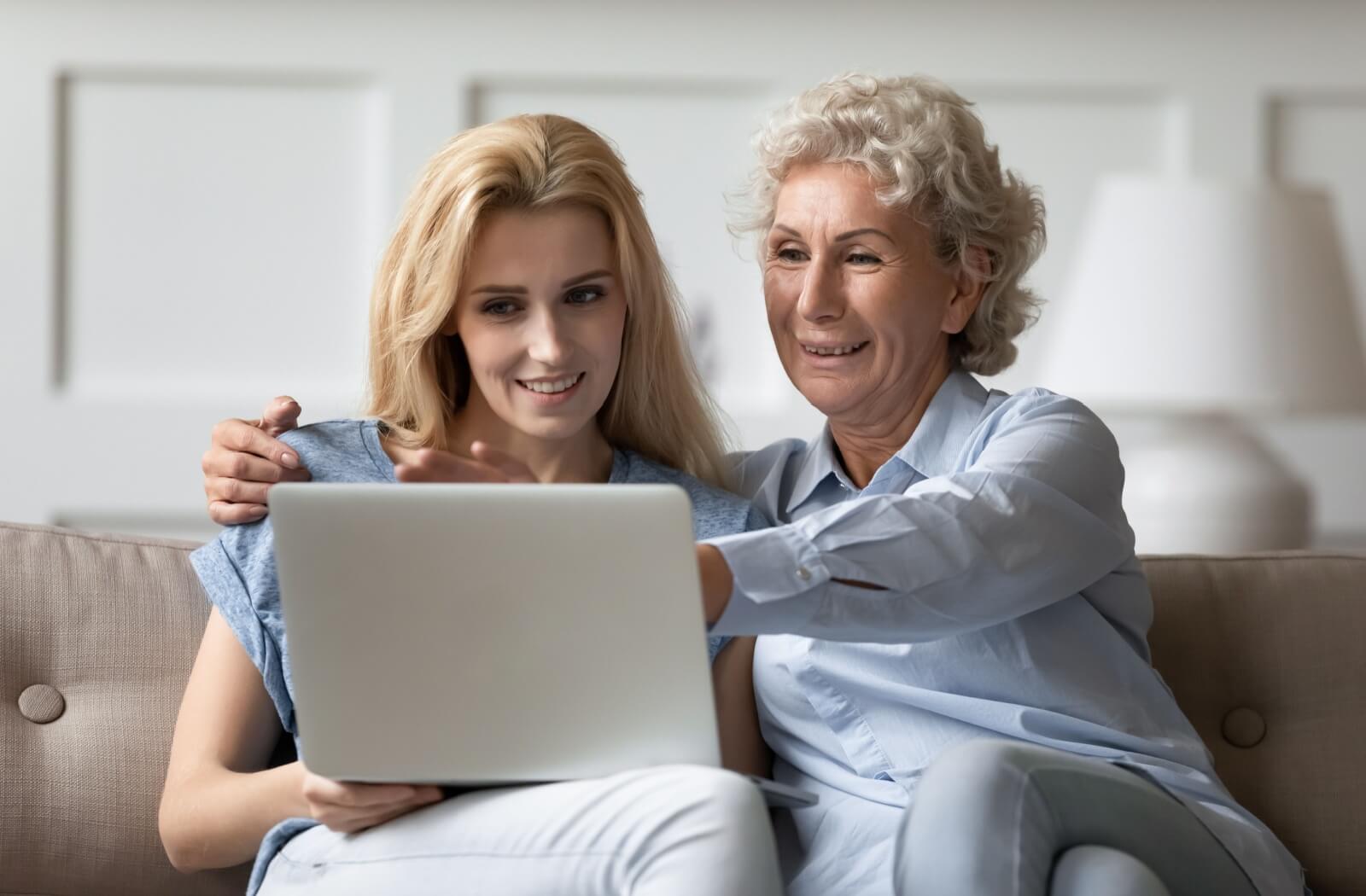 A happy senior looks at senior memory care community options for the future with their adult child on the computer.