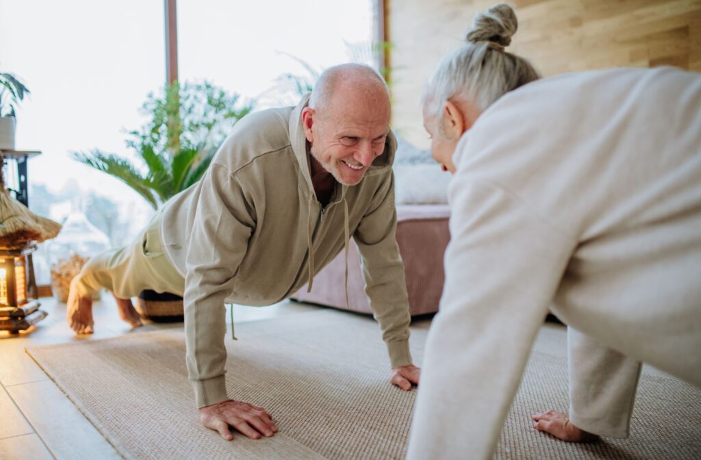 A smiling older couple exercising together in the living room.