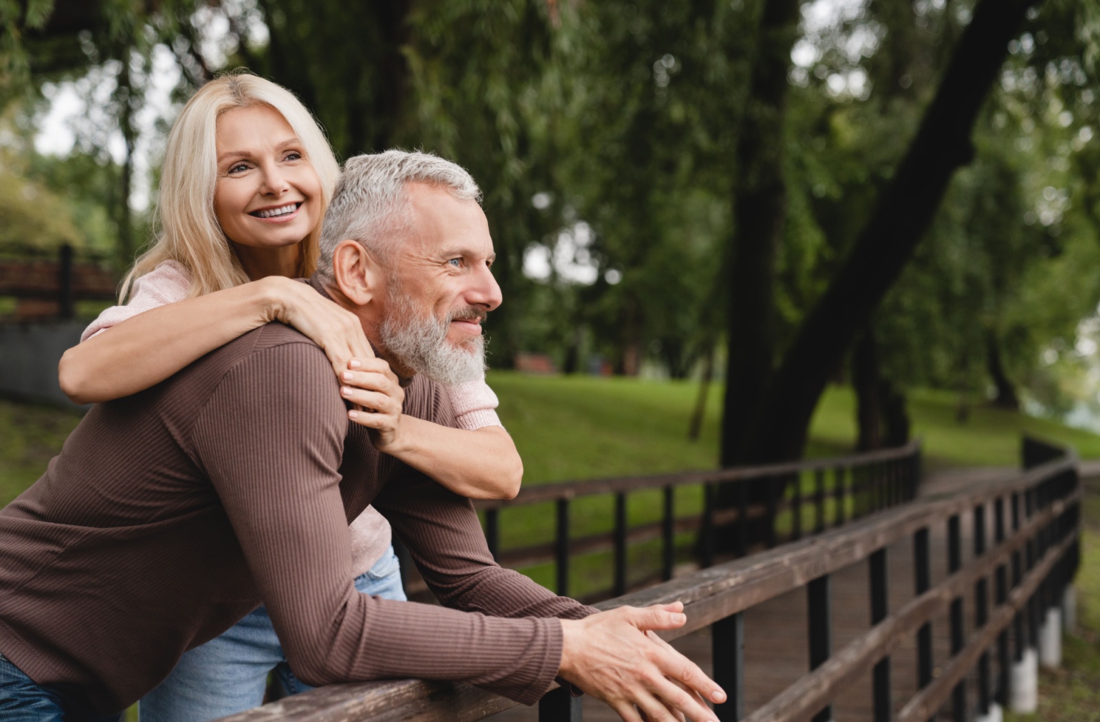 A happy older couple standing at a bridge in a park.