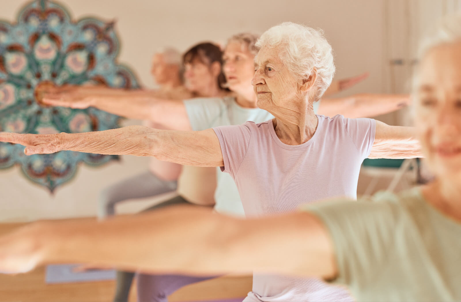 A group of older adults stretching their arms out wide in a yoga pose during an exercise class.