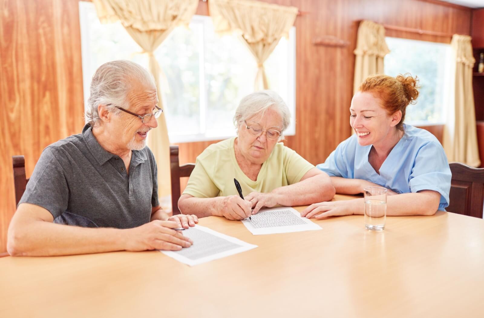 A nurse helps two seniors with dementia complete a memory game to help keep their cognitive skills engaged