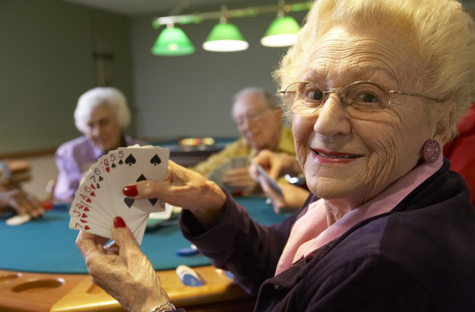 A happy senior in a personal care home showing a card of hands during a game with other residents