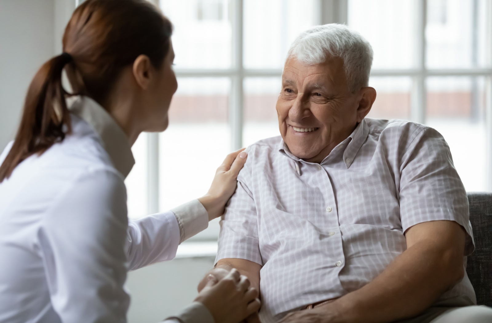 An older adult with dementia smiling at a caregiver and holding their hand in a memory care community.
