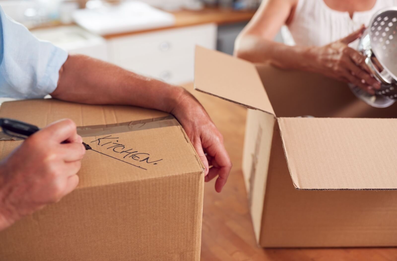 A close-up of an older man writing a label on a moving box of kitchen supplies