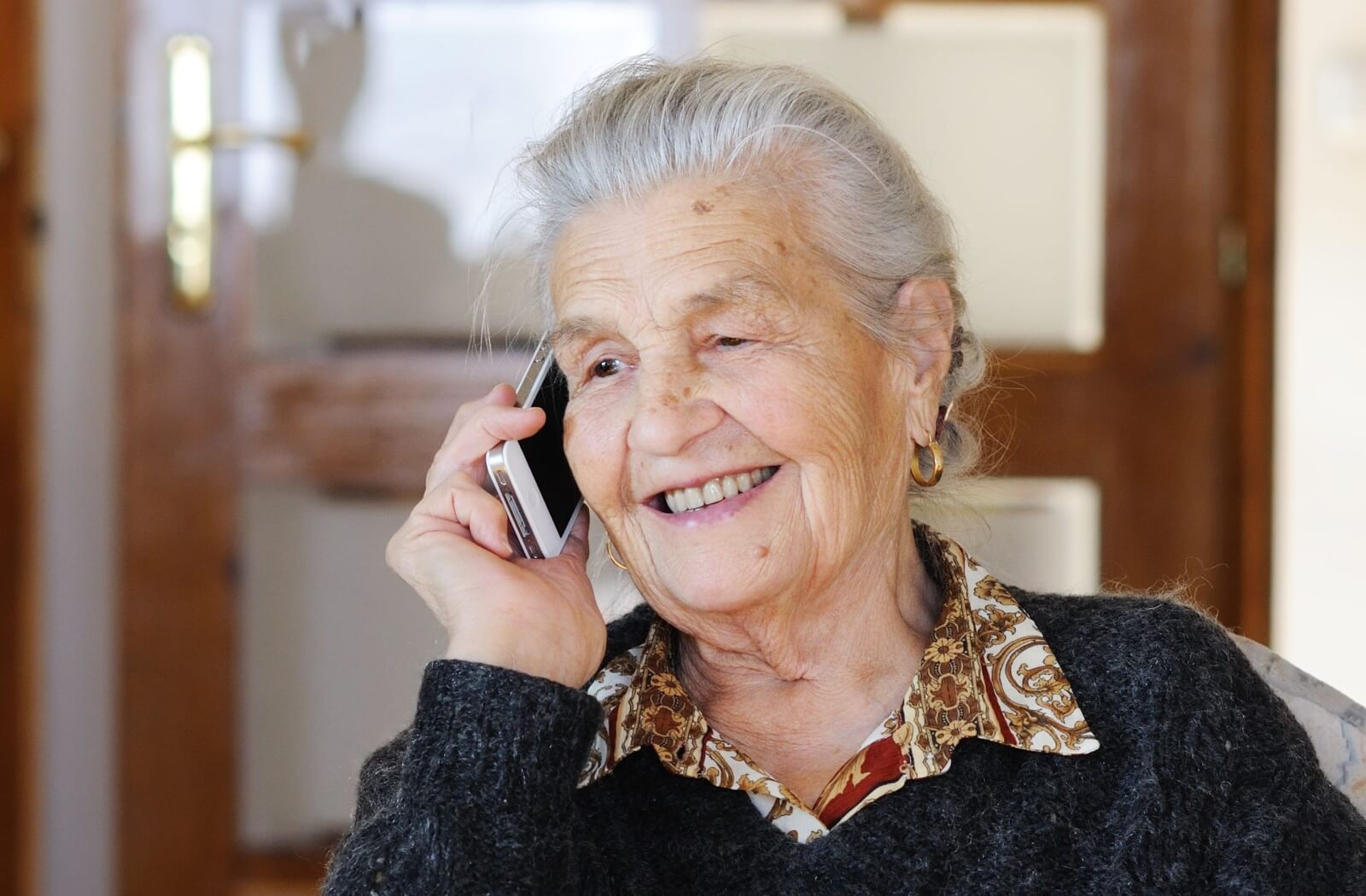 A happy older adult woman with dementia on her phone talking to a loved one.