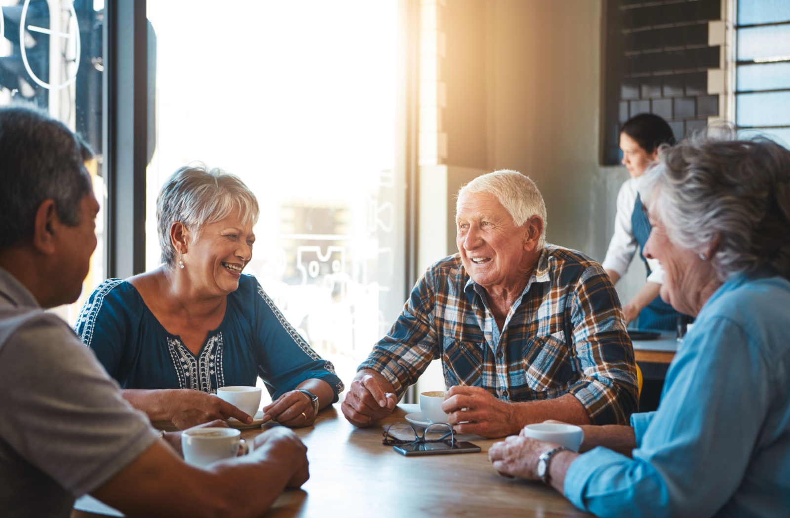 A group of older adults laughing together in a sunlit coffee shop, laughing and chatting.