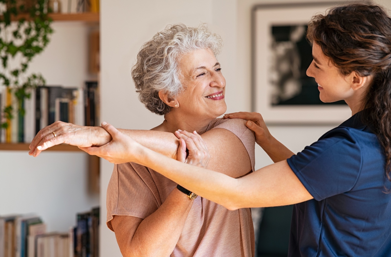 An older adult smiling as a caregiver adjusts their arm during a workout in senior living.