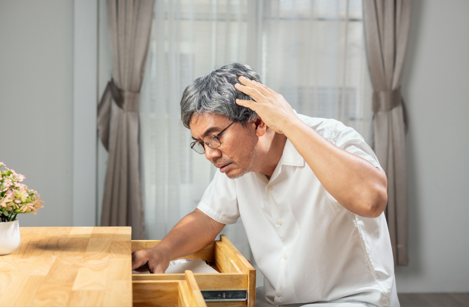 A confused senior with dementia looks for clothing in a dresser that is stuffed full of paper