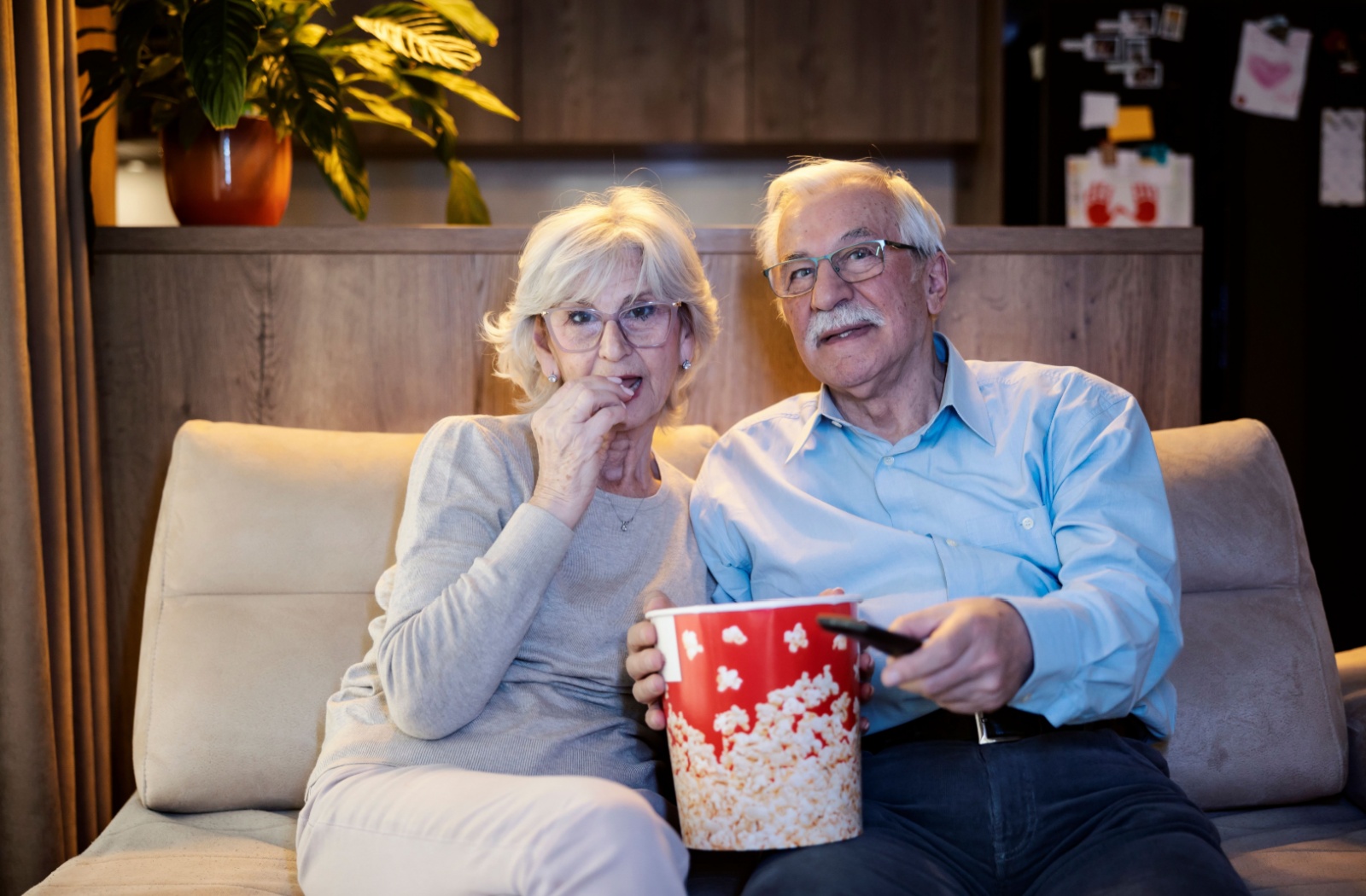 A senior couple shares a bucket of popcorn while watching a movie