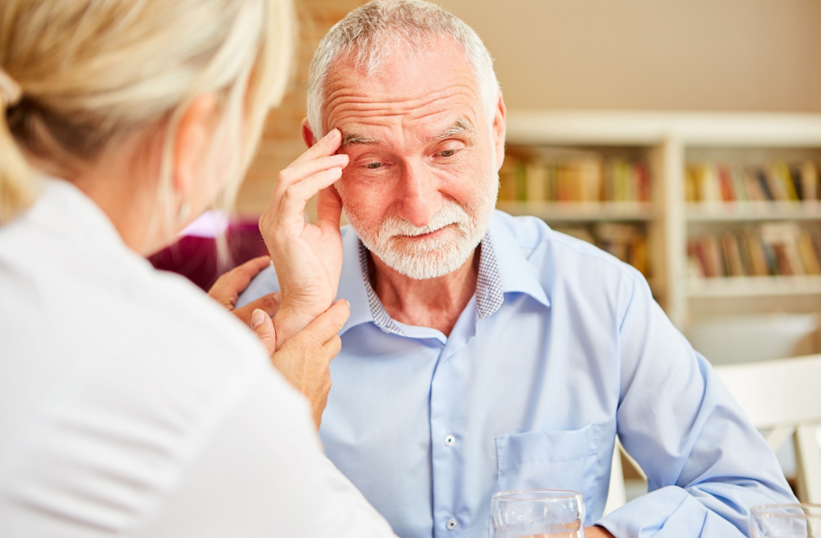 An older adult touches their forehead during a healthcare checkup to discuss their recent confusion